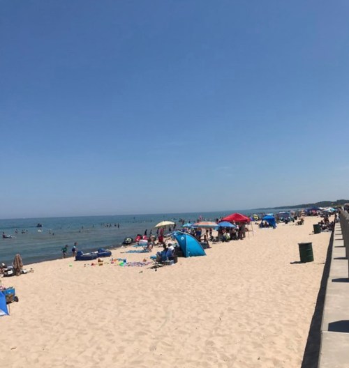 A sunny beach scene with people enjoying the water, colorful umbrellas, and a sandy shore under a clear blue sky.