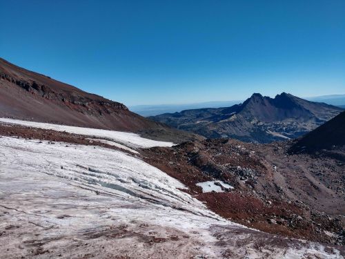 A panoramic view of a mountainous landscape with snow and rocky terrain under a clear blue sky.