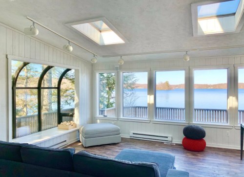 Bright sunroom with large windows overlooking a lake, featuring a cozy couch and modern decor.