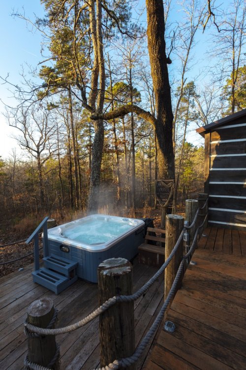A hot tub with steam rising, surrounded by trees and wooden decking in a serene outdoor setting.