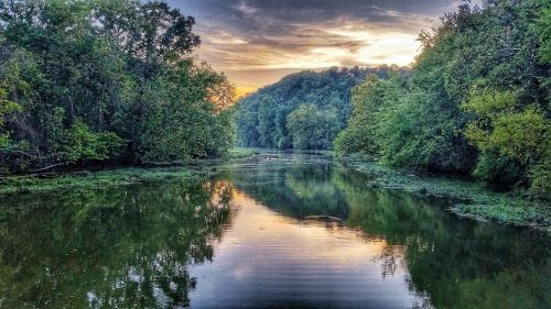 A serene river scene at sunset, surrounded by lush greenery and reflecting the colorful sky.