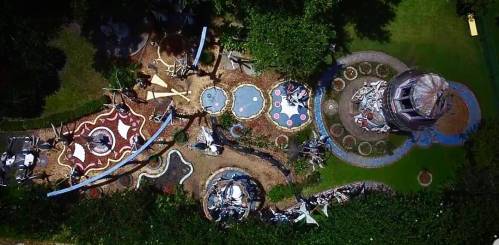 Aerial view of a whimsical garden featuring colorful pathways, sculptures, and a circular pond surrounded by greenery.