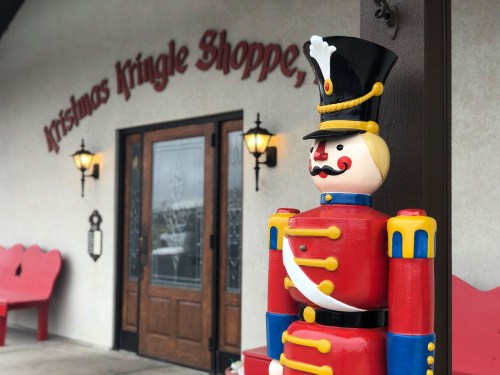 A colorful toy soldier stands outside the Christmas Kringle Shoppe, with festive signage and a welcoming entrance.