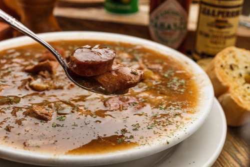 A spoonful of hearty soup with sausage and herbs, served in a bowl alongside a slice of bread.