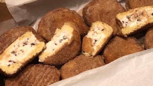 A tray of golden-brown fried treats, some whole and others cut open, revealing a creamy filling with chocolate chips.
