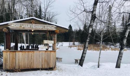 A wooden kiosk at Chip Willet Memorial Pond, surrounded by snow and trees, with a frozen pond in the background.