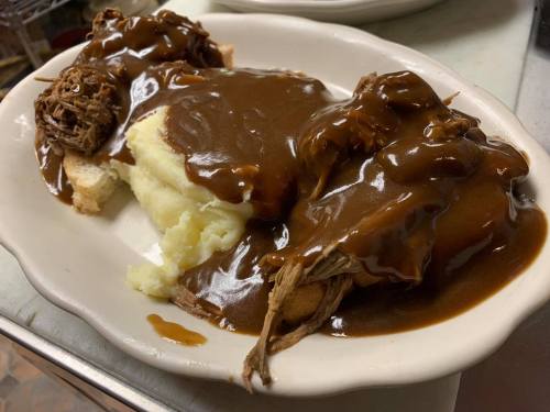A plate of mashed potatoes topped with shredded beef and brown gravy, served on slices of bread.