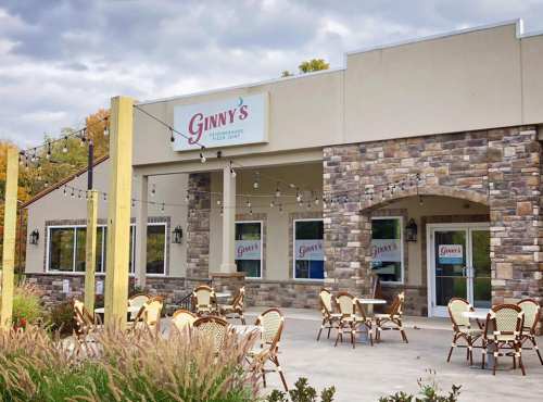 Exterior of Ginny's pizzeria featuring a stone facade, outdoor seating, and string lights under a cloudy sky.