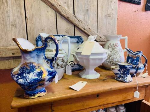 A collection of vintage ceramic pitchers and a decorative bowl displayed on a wooden table against a rustic background.