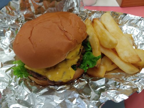A cheeseburger with lettuce in a bun, wrapped in foil, served with a side of golden French fries.