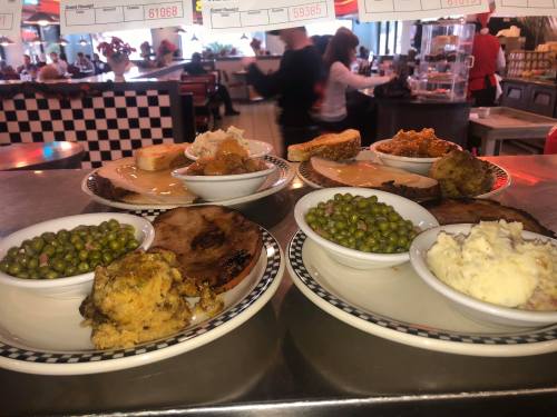 Two plates of comfort food featuring meat, mashed potatoes, green peas, stuffing, and bread in a diner setting.