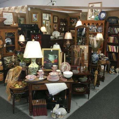A cozy antique shop display featuring vintage lamps, dishes, and decor arranged on wooden tables and shelves.