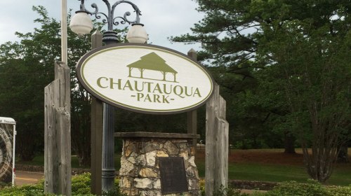 Sign for Chautauqua Park, featuring a gazebo design, surrounded by trees and greenery.