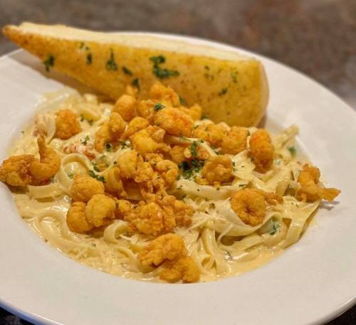 A plate of fettuccine alfredo topped with crispy shrimp and served with a slice of garlic bread.