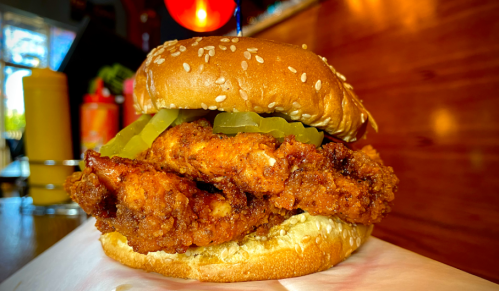 A close-up of a sesame seed bun sandwich filled with crispy fried chicken and pickles.