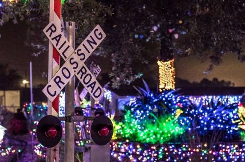 A railroad crossing sign illuminated by colorful holiday lights in a festive nighttime setting.