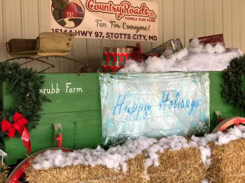 A festive display with a green cart, holiday decorations, and a sign reading "Happy Holidays" at a family fun farm.