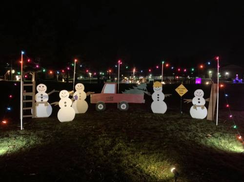 A festive display featuring snowmen, a red truck, and colorful lights in a nighttime setting.