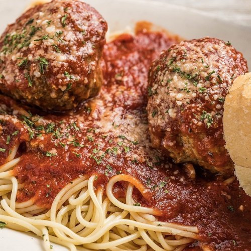 A plate of spaghetti topped with marinara sauce, two meatballs, grated cheese, and a slice of bread on the side.