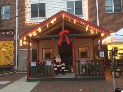 A festive Santa Claus sits in a decorated wooden hut with holiday lights and ornaments.