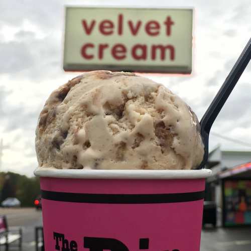 A close-up of a cup of ice cream with a sign in the background that reads "velvet cream."