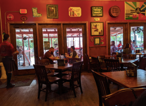 A cozy restaurant with red walls, wooden tables, and patrons dining inside and outside. A server is walking by.
