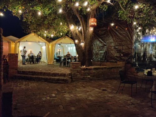 Cozy outdoor dining area with illuminated tents, string lights, and a tree, creating a warm evening atmosphere.