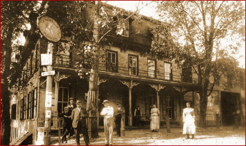 Historic building with people outside, featuring a porch and trees, captured in a vintage black-and-white style.