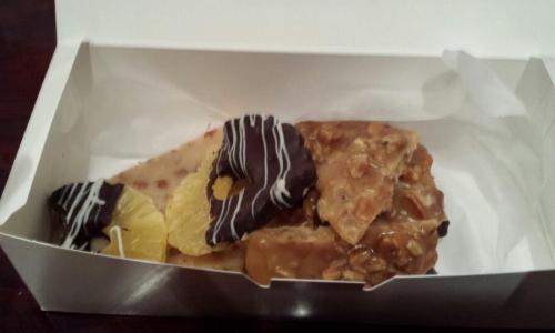 A box containing assorted treats: chocolate-covered fruit, nut brittle, and caramel candy.