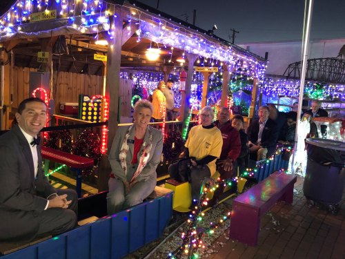 A group of people sitting on a colorful train ride decorated with festive lights at night.