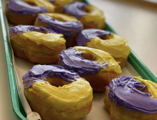 A tray of donuts with yellow and purple frosting, arranged neatly on a white surface.