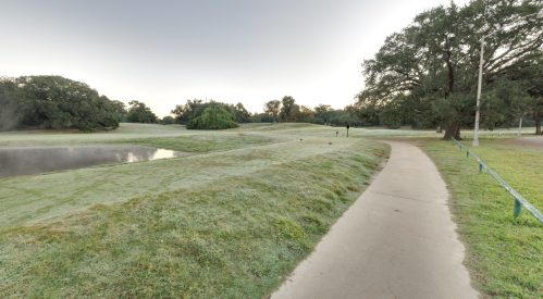 A serene golf course at dawn, featuring a misty landscape, a pond, and a winding path surrounded by trees.