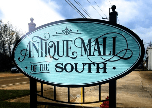 Sign for "Antique Mall of the South" with a decorative blue background and cloudy sky above.