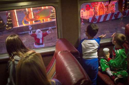 Children in festive pajamas watch Santa outside a train window, surrounded by colorful holiday decorations.