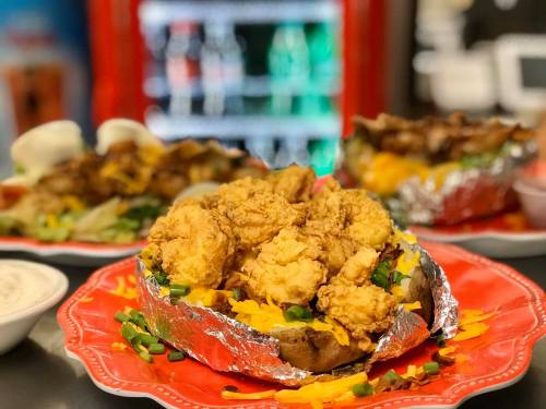 A loaded baked potato topped with fried shrimp, cheese, and green onions, served on a red plate.