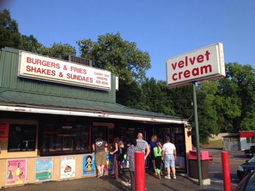 A busy burger and ice cream stand with a sign reading "Velvet Cream" and a line of customers outside.
