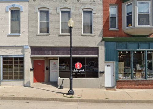 Exterior of a storefront labeled "club geek," featuring a sign that says "open," with nearby buildings visible.