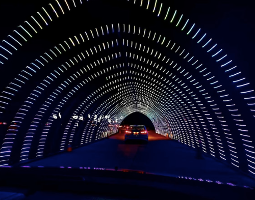 A car drives through a brightly lit tunnel with colorful, glowing patterns on the walls.