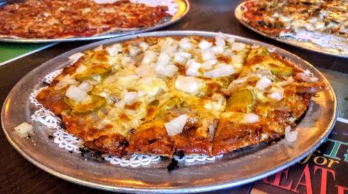 A close-up of a pizza topped with cheese, onions, and green peppers on a silver platter, with other pizzas in the background.