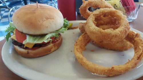A plate with a cheeseburger topped with lettuce, tomato, and pickles, alongside crispy onion rings.