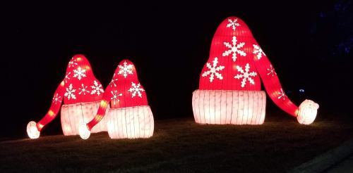 Three large illuminated red Christmas hats with white snowflakes, set against a dark background.