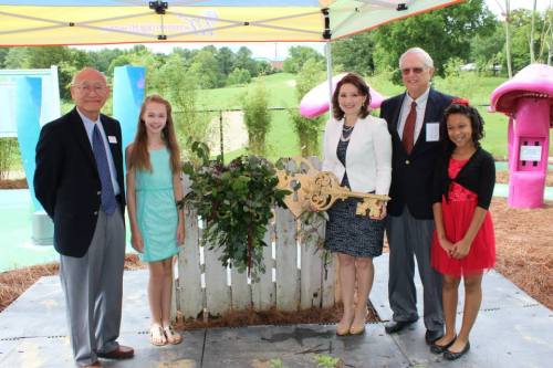 A group of five people, including children and adults, pose with a large decorative key at an outdoor event.