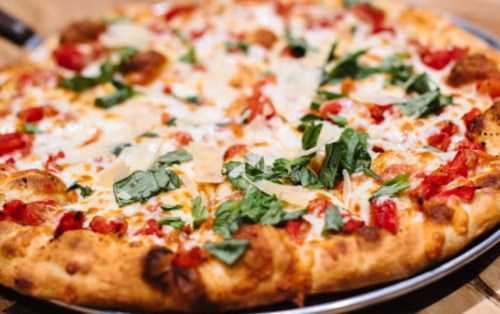A close-up of a freshly baked pizza topped with cheese, tomatoes, and fresh spinach on a metal tray.
