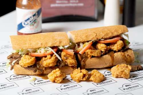 A delicious sandwich filled with fried shrimp, lettuce, and tomato, served on a toasted hoagie roll with a bottle of hot sauce.