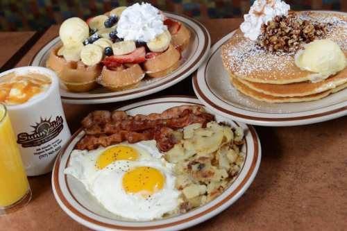 A delicious breakfast spread featuring waffles, pancakes, eggs, bacon, and hash browns, with a drink on the side.
