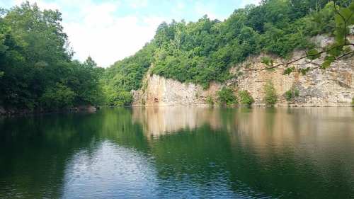 A serene lake surrounded by lush green trees and rocky cliffs, reflecting the landscape in calm waters.