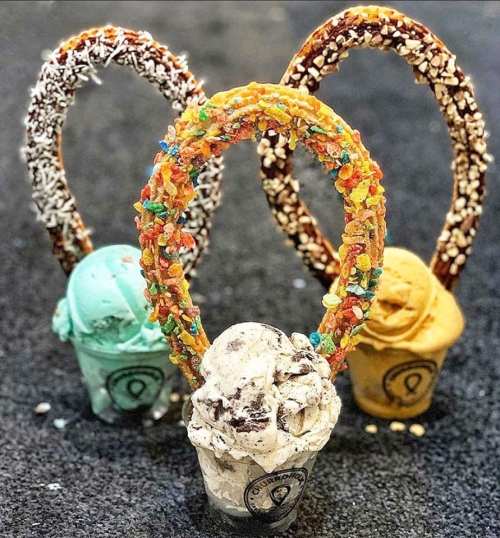 Three colorful ice cream cones topped with candy and surrounded by pretzel loops, set against a dark background.