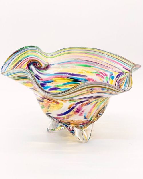A colorful, swirled glass bowl with a wavy rim and clear feet, showcasing vibrant hues of pink, blue, yellow, and green.