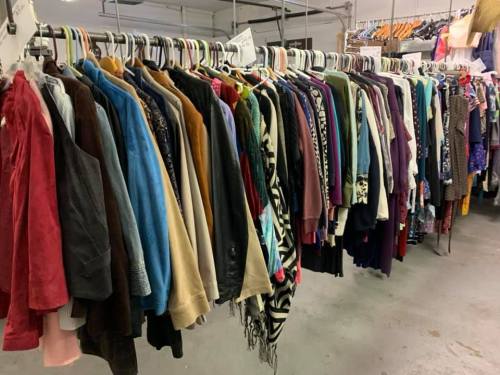 A row of colorful clothing hanging on racks in a thrift store, showcasing various styles and fabrics.