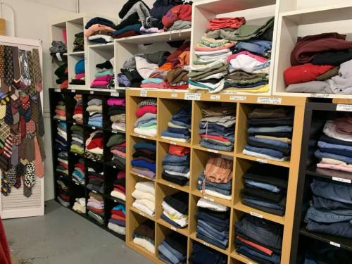 A neatly organized room with shelves filled with folded clothes and stacks of sweaters and jeans.